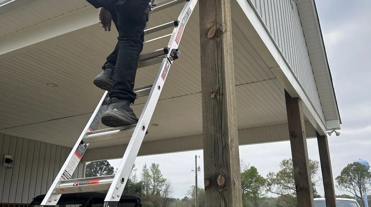Dubya Roofing crew member installing seamless gutters on ladder at Rowesville SC home